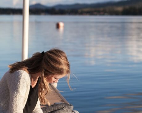 photo of woman reading book near body of water