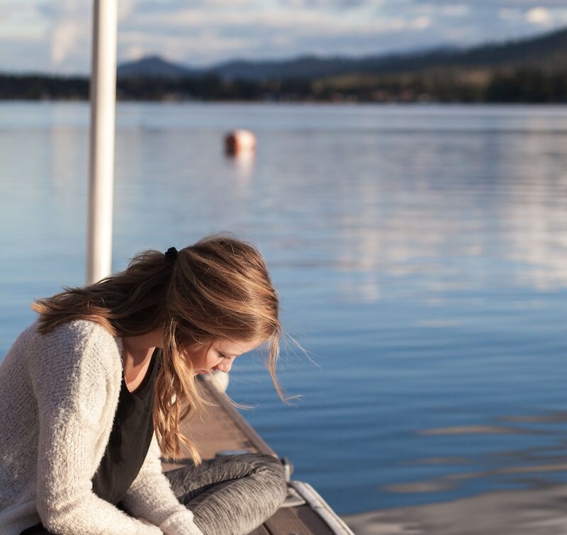 photo of woman reading book near body of water